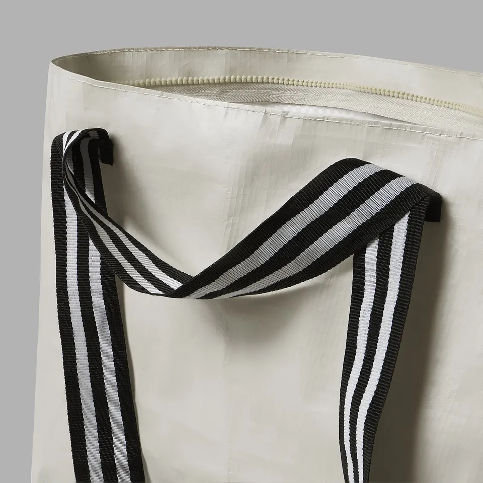 Close-up of a sturdy white tote bag with black and white striped handles, showcasing quality stitching and design.