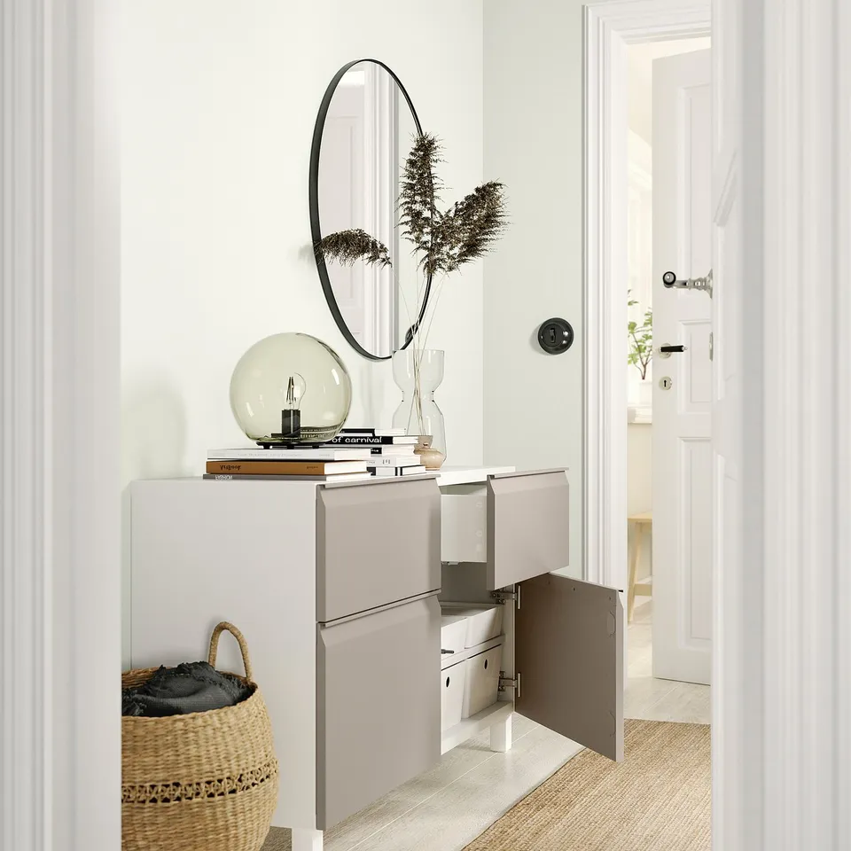 Modern white BESTÅ sideboard with open doors revealing storage compartments and shelves, topped with decorative items.