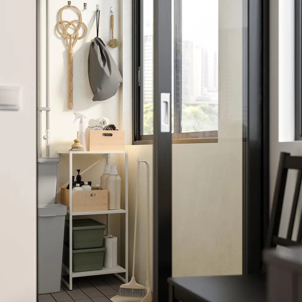 Small white metal storage unit in bathroom with cleaning supplies, hooks with items, near window; part of JOSTEIN system.
