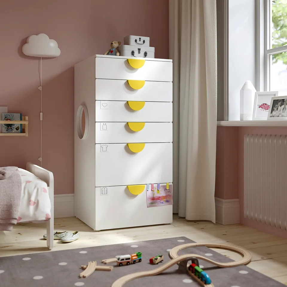 Childs room with white ikea SMÅSTAD chest. Six drawers, yellow handles, standing tall by window.