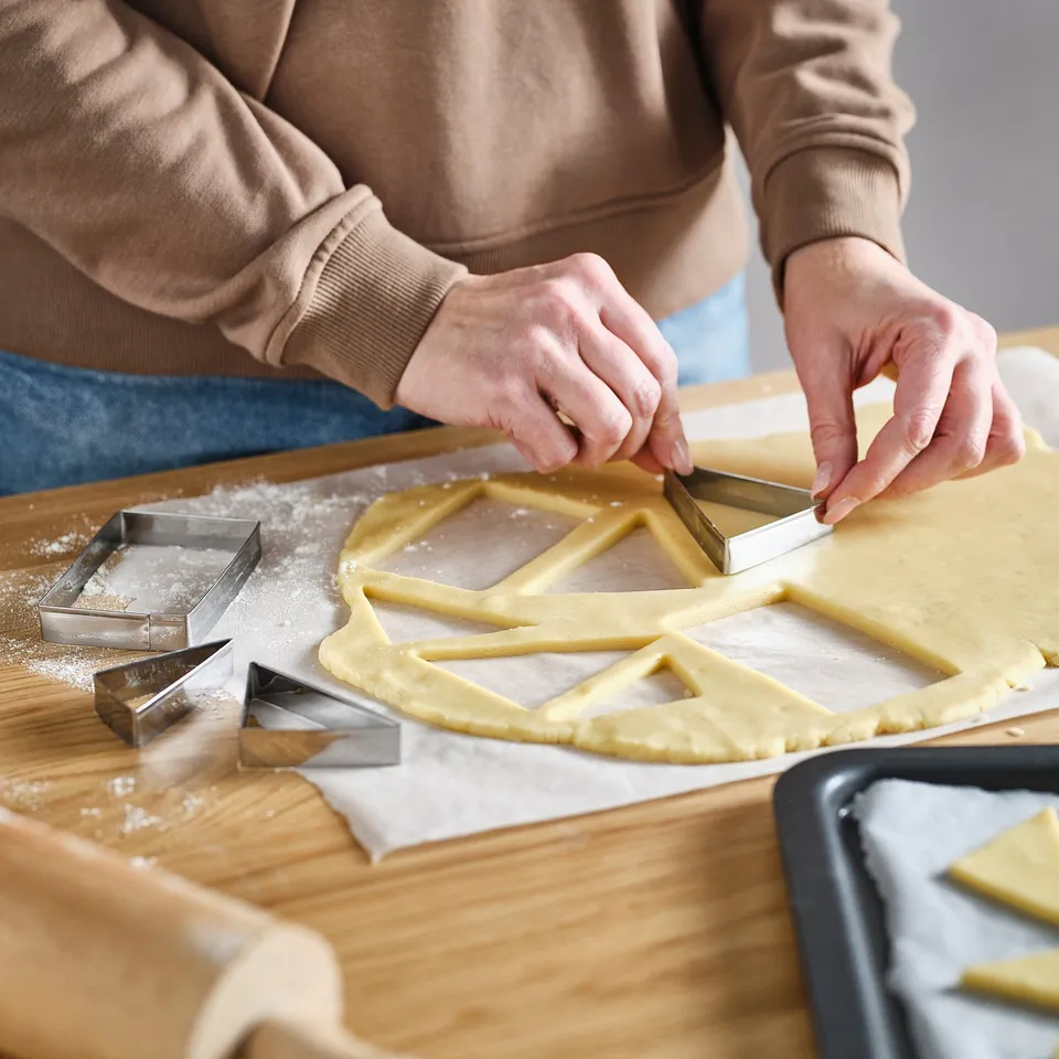 Person uses cookie cutters to shape dough into geometric patterns on a wooden board.