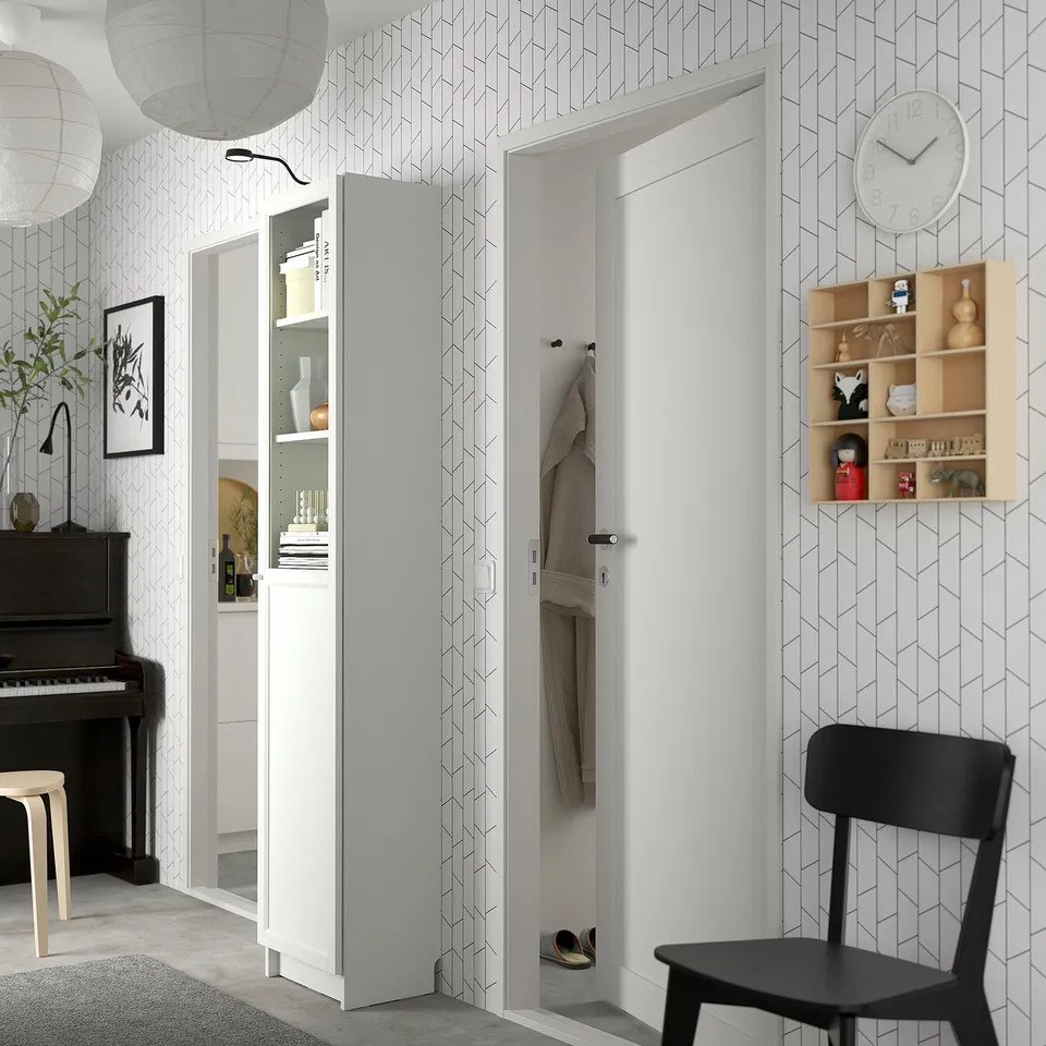 Modern entryway with white BILLY bookcase, black chair, geometric wallpaper, and piano.