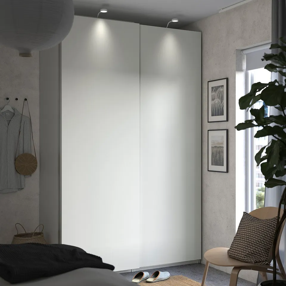 Modern bedroom with white sliding closet doors, soft lighting, minimalist decor, striped shirt, white slippers, chair, plant, and framed art.