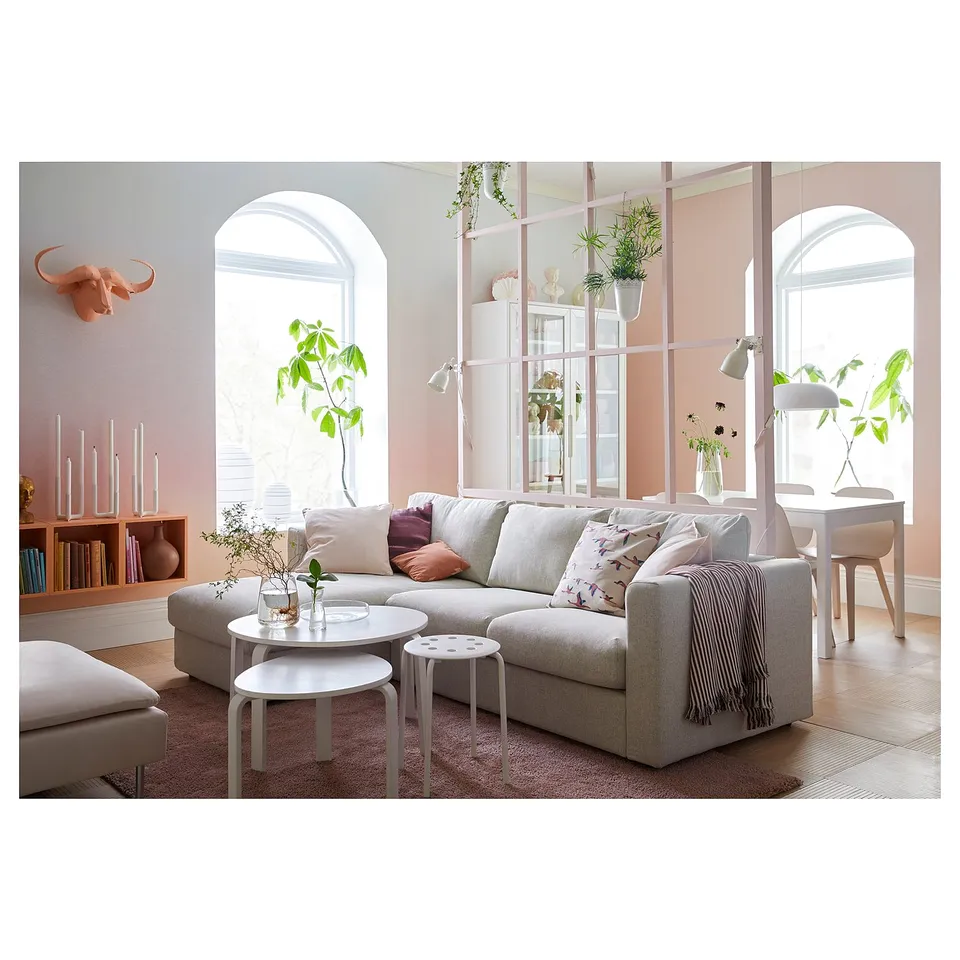 Modern living room with VIMLE beige sofa-bed, white coffee table, pink pillows, and plants.