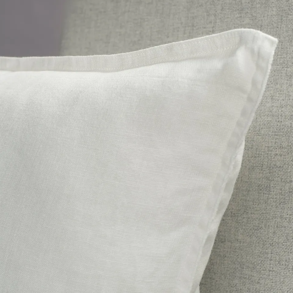 Close-up of crisp, white linen cushion cover on textured fabric, showcasing soft texture and neat stitching.