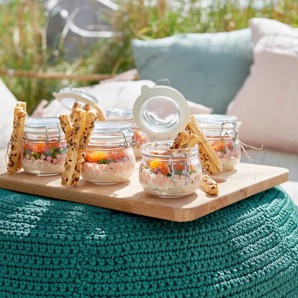 Glass jars with lid, layered salads, sticks on wooden board outdoors.