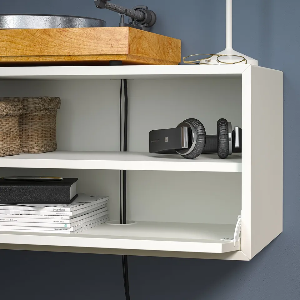 White EKET shelving unit mounted on wall, holding books, vr headset, and basket.