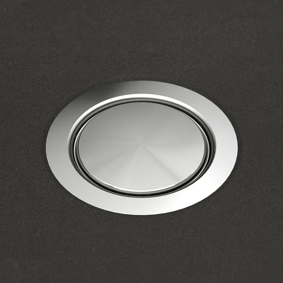 A sleek, stainless steel sink drain cover set into a smooth, dark quartz composite sink, showcasing high-quality craftsmanship.