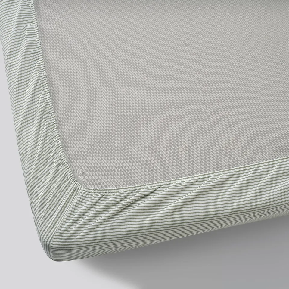 Close-up view of a white cotton mattress cover with striped elastic edges, showcasing its quality and design.