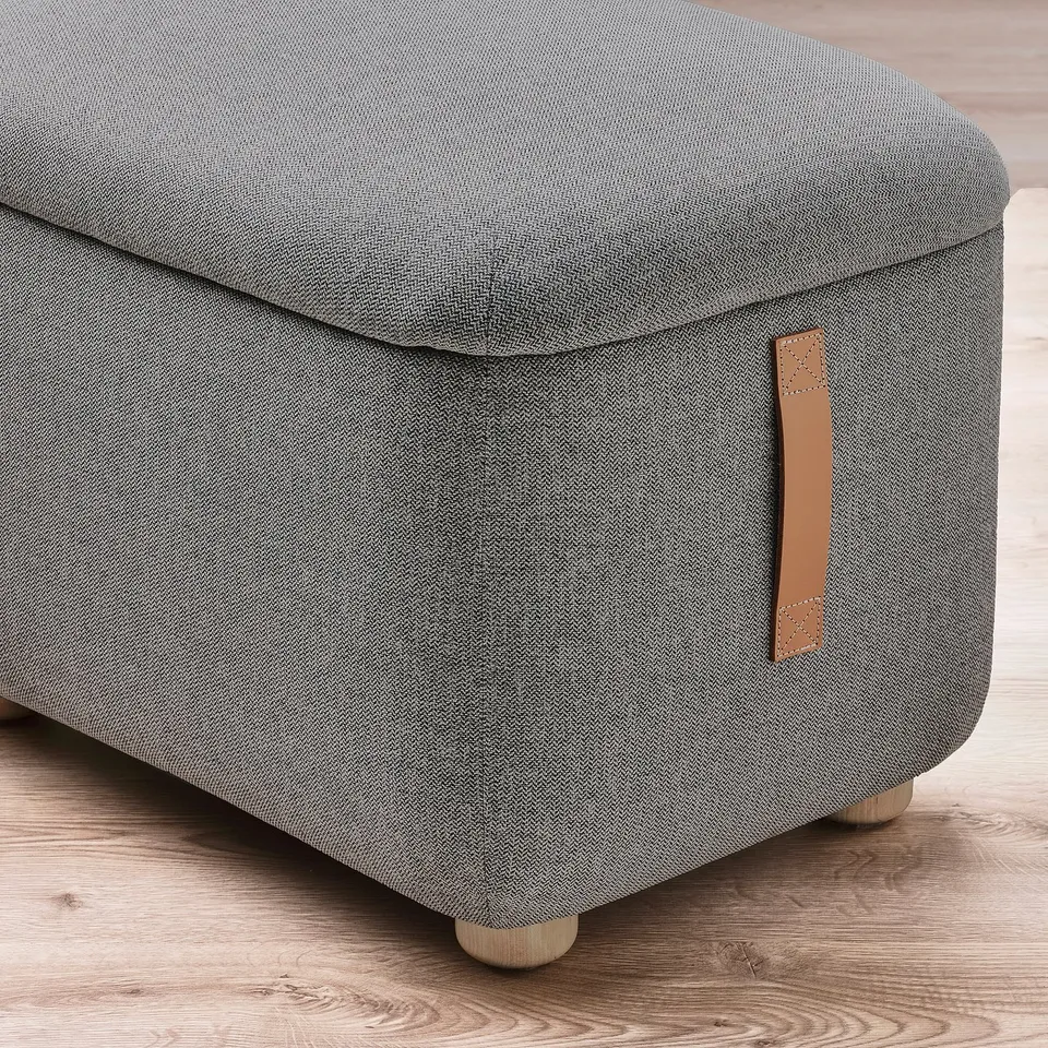 Plush grey footstool with leather handle and wooden legs.