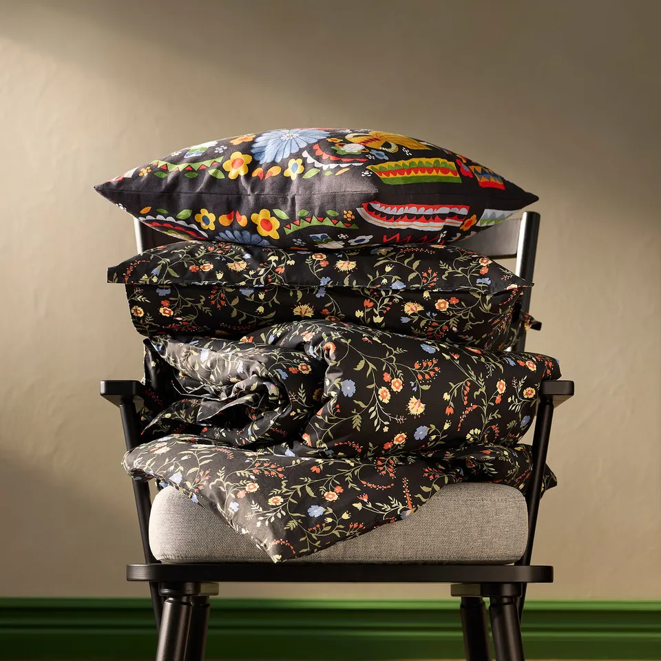 Three black pillows with floral patterns stacked on a black chair against a beige wall.