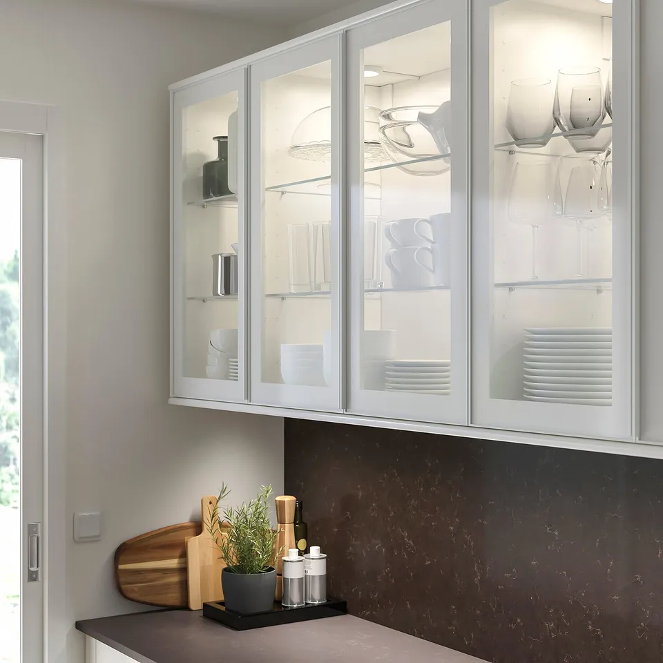 Modern kitchen with HEJSTA cabinets, glassware, dark countertop, wooden board, utensils, sleek design, marble backsplash.