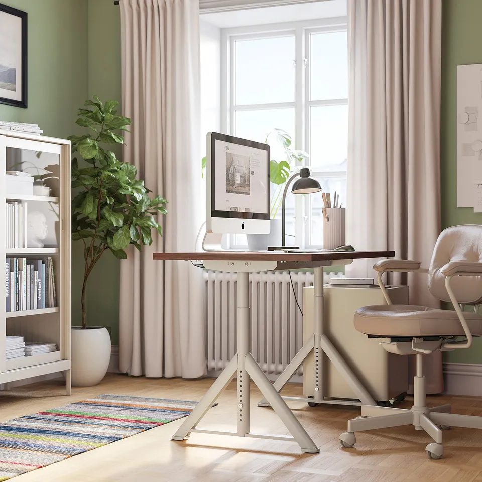 Home office with adjustable IDÅSEN desk, imac, supplies, large window, bookshelf, and chair.