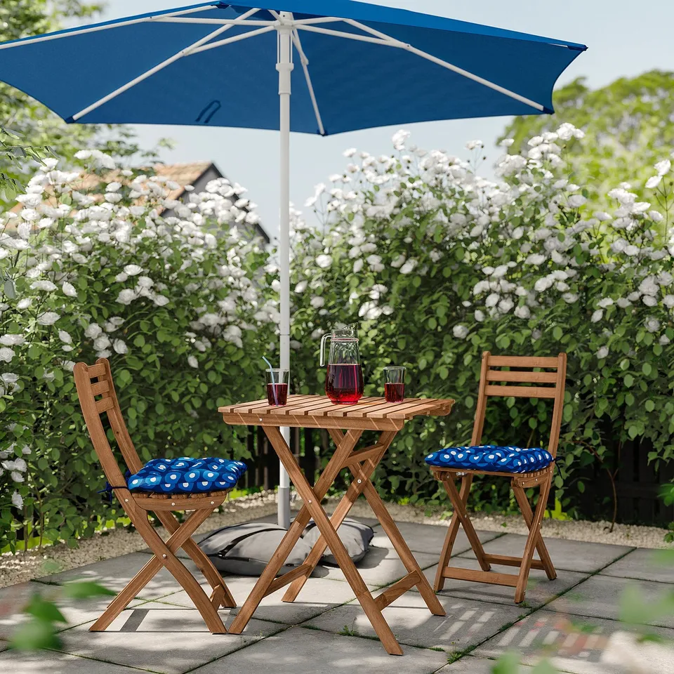 Small outdoor patio set with blue umbrella and cushioned chairs, perfect for relaxation.