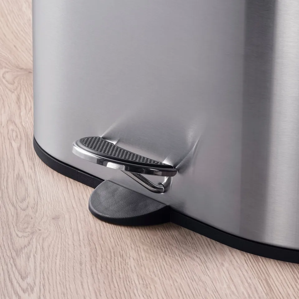 Stainless steel pedal bin with soft-close mechanism on wooden floor.