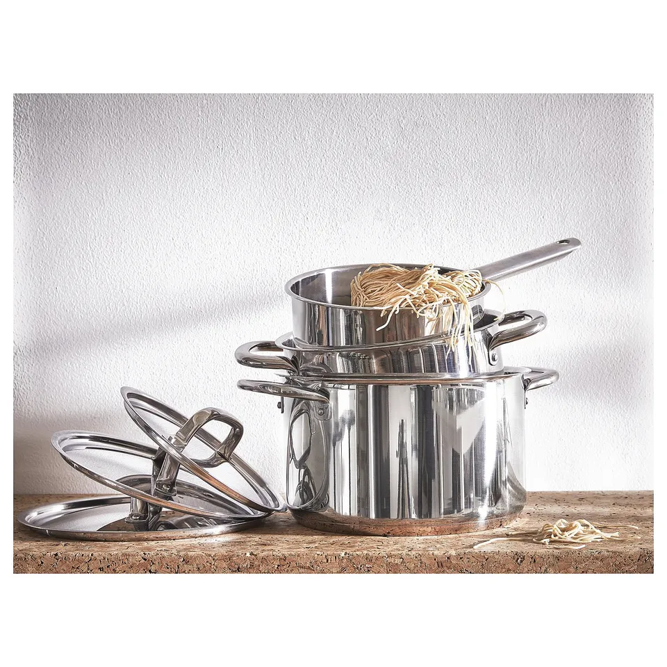 IKEA 365+ stainless-steel pots with handles, lids, and noodles inside, stacked neatly on a wooden surface.