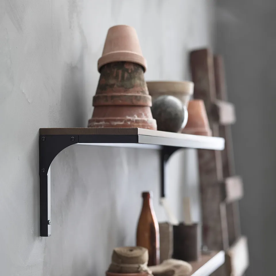 Industrial-style rustic wall shelf with metal brackets, holding assorted terracotta planters and vases.