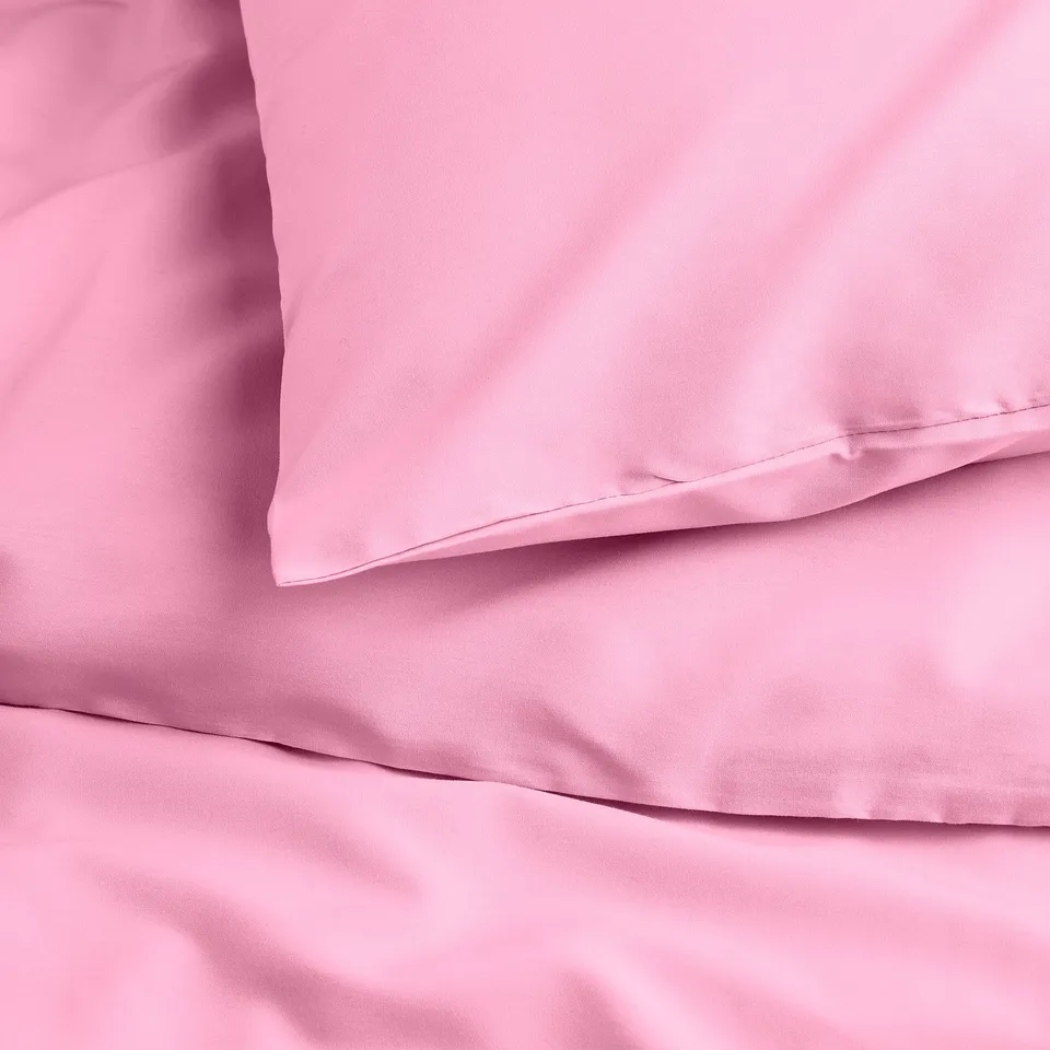 Light pink bedding, smooth and soft, intricate folds and a plush pillowcase, showcasing quality and comfort.