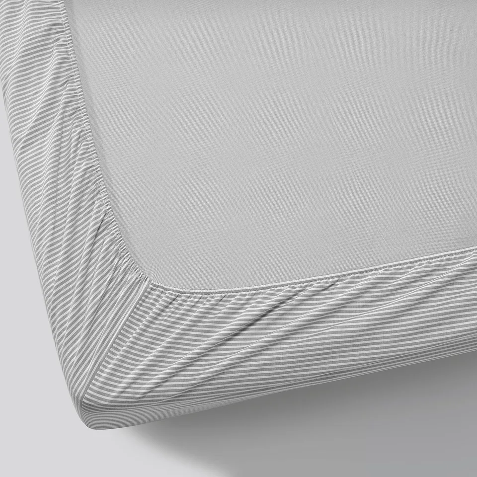 Grey fitted sheet with striped edges, perfectly fitted on a mattress, showcasing quality cotton material.