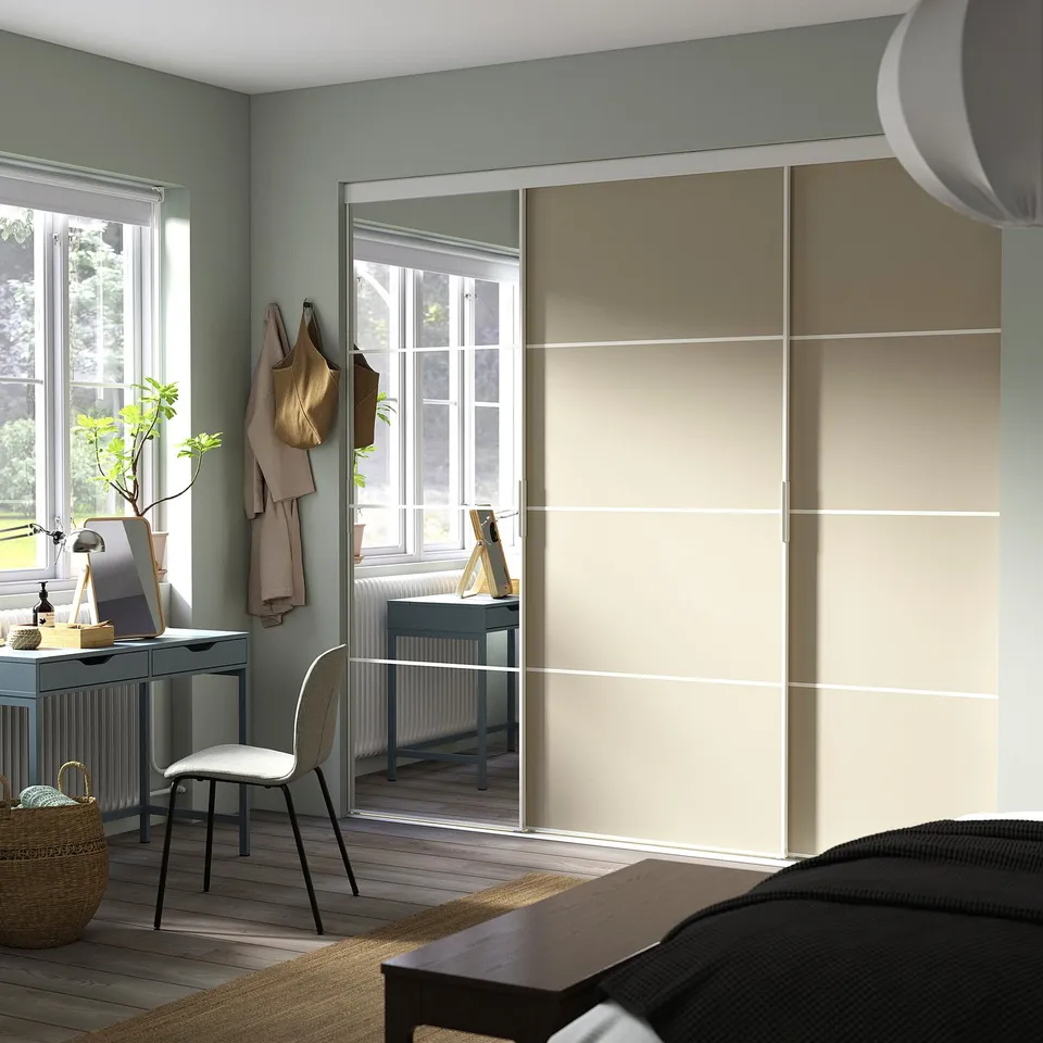 Modern home office in light green room with large wardrobe, wooden floors, desk, chair, plant, and lamp.