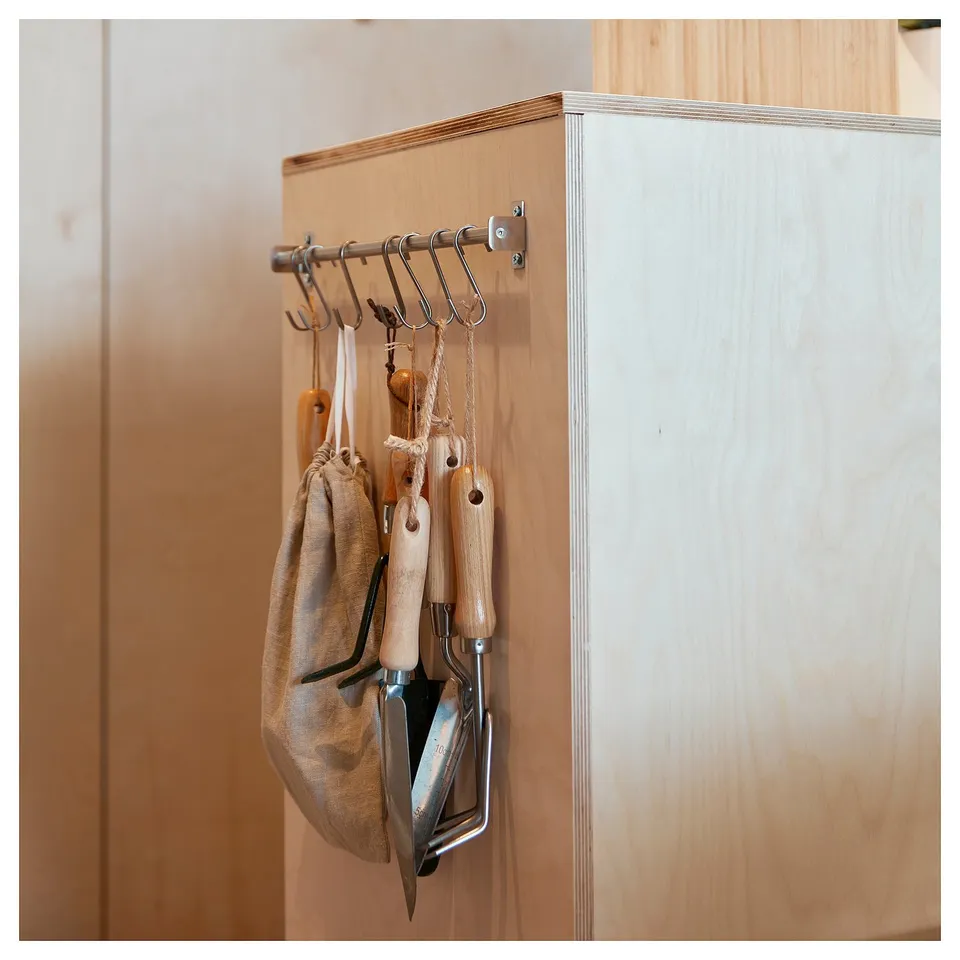 KUNGSFORS stainless-steel rail with s-hooks, holding wooden kitchen tools and a jute bag, mounted on a wooden wall.