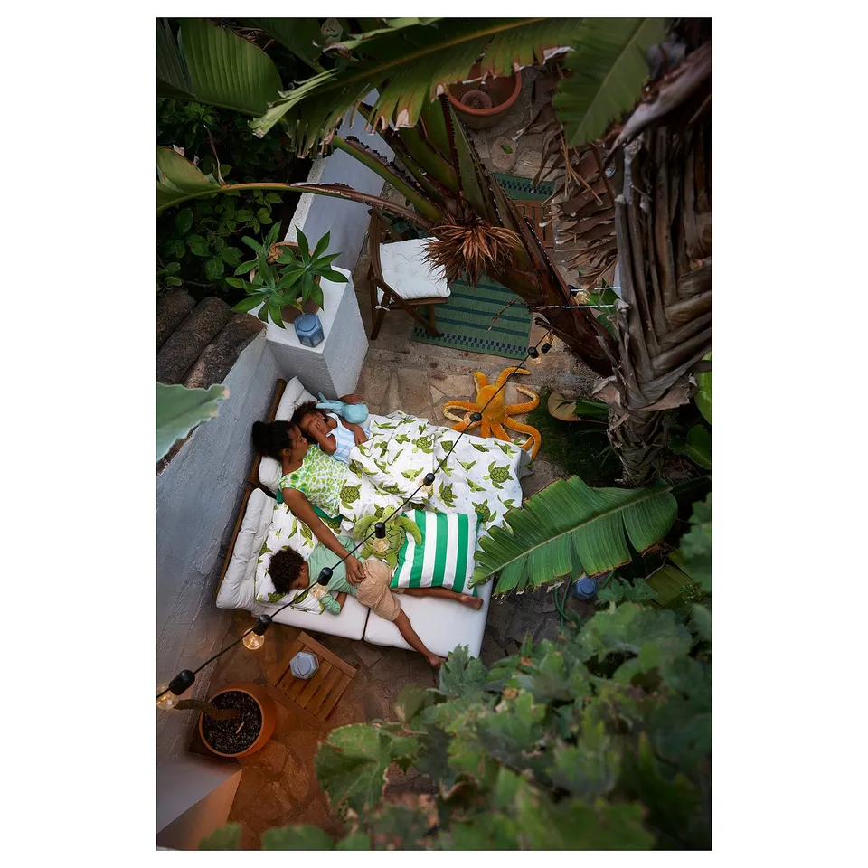 Outdoor relaxing zone with NÄMMARÖ furniture. Colourful cushions, lush plants. Wooden frame. Natural, inviting design.
