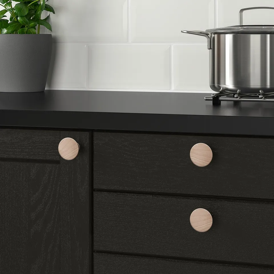 Black kitchen drawers with wooden knobs, plant nearby. Alternative: black drawers with wooden knobs, plant on dark counter.