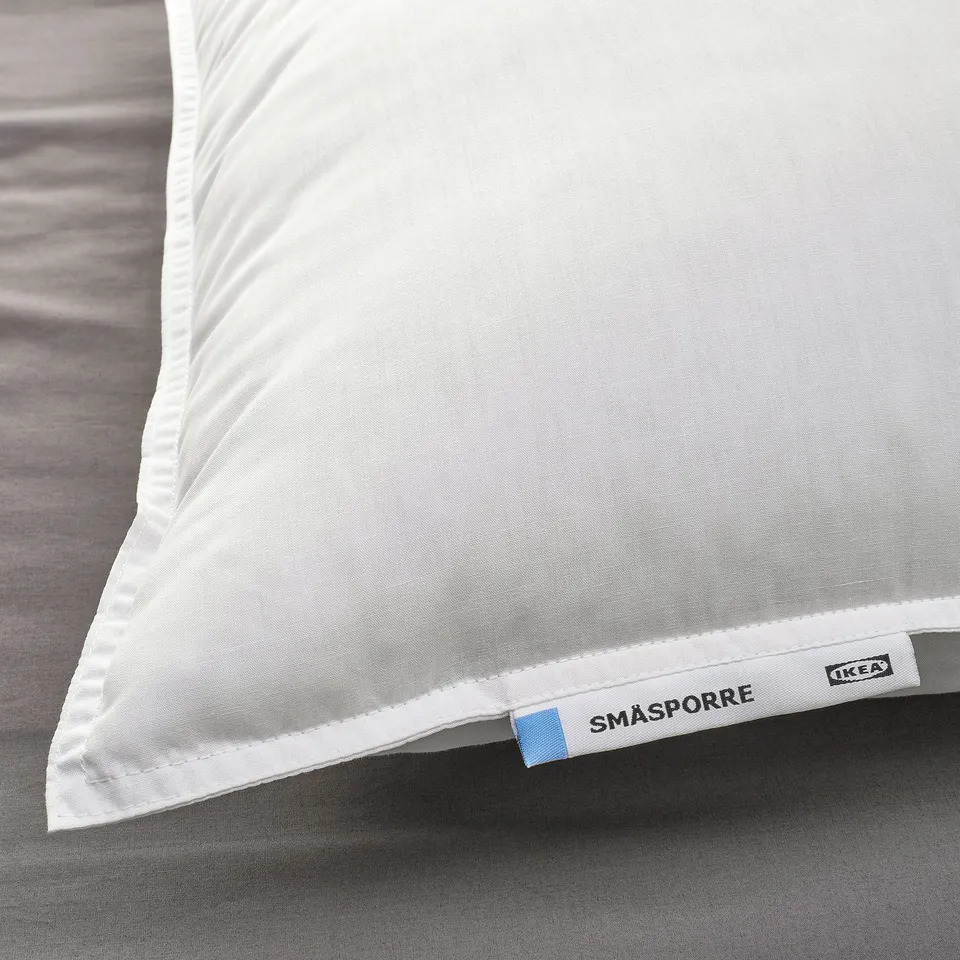White pillow on bed, soft and firm, with IKEA tag SMÅSPORRE.