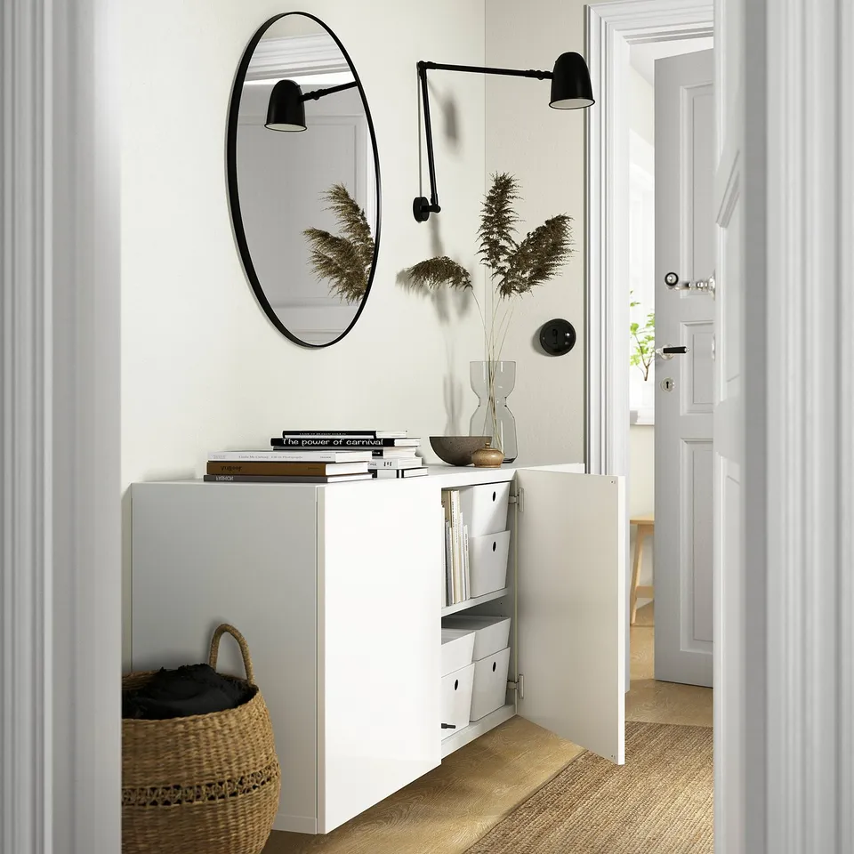 White BESTÅ cabinet with adjustable shelves and soft-close drawers. Vase, books, and lighting are on top, with a woven basket below.