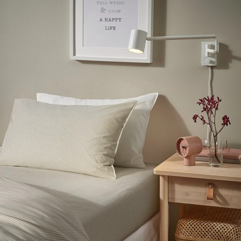Cosy bedroom with SOLFIBBLA pillow, vase, alarm clock, and wall light.