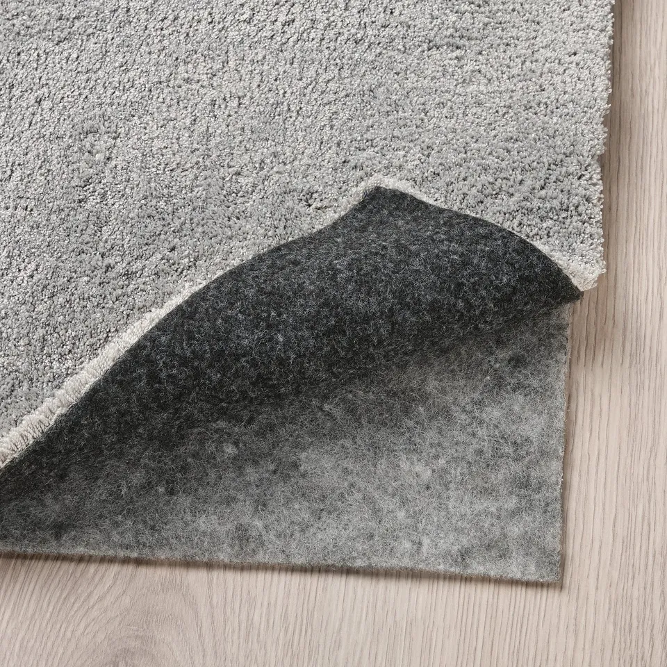 Grey rug corner on light wooden floor. Shiny, soft pile shown, ideal for comfort and sound dampening.
