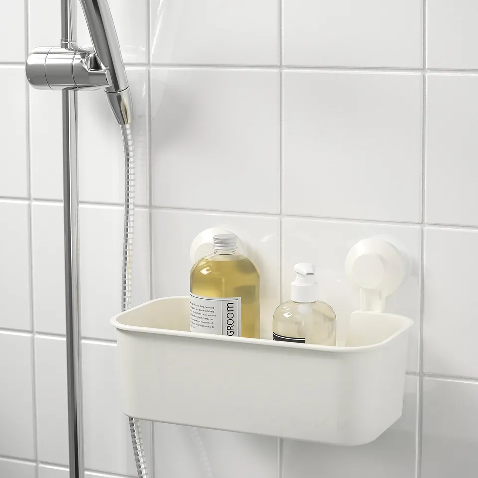 A white bathroom caddy on a tiled wall, holding grooming products. Showerhead visible to left.