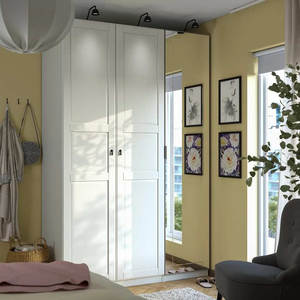 Modern bedroom with large PAX wardrobe, mirrored doors, wall decorations, blue chair, hanging purse, clothes.
