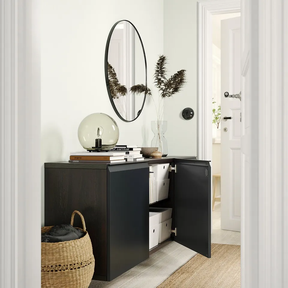 Modern hallway featuring a black BESTÅ cabinet, round wall mirror, and woven basket with dried plants.