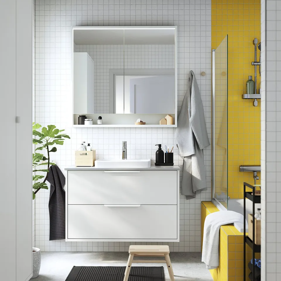 Modern bathroom with white TOLKEN vanity, large mirror, yellow tiles, and grey towels.