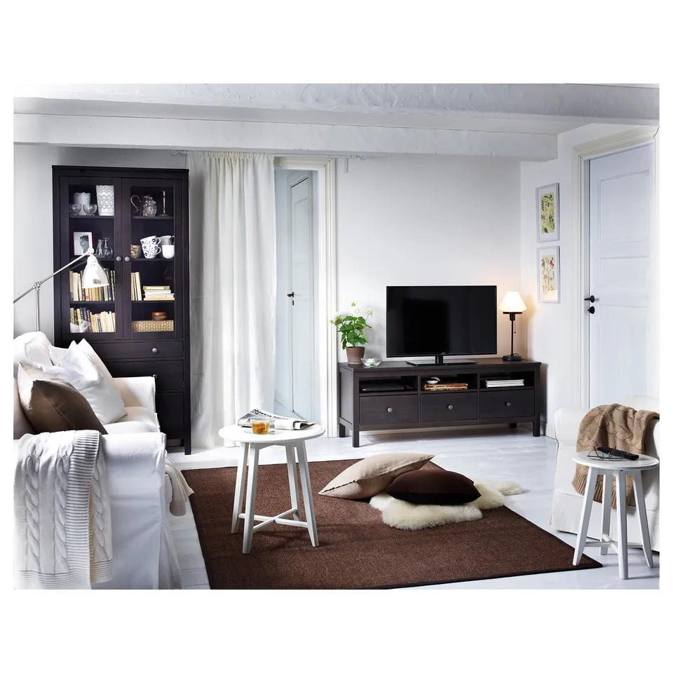 Modern living room with white sofa, coffee table, black tv stand, and glass cabinet. Bright and cosy with rug, plants, and decor.