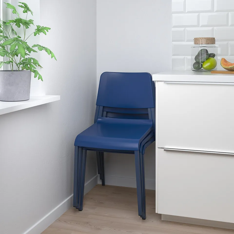 Blue stacking chair, TEODORES, set against white cabinet and wall with shelf holding plant and fruits.