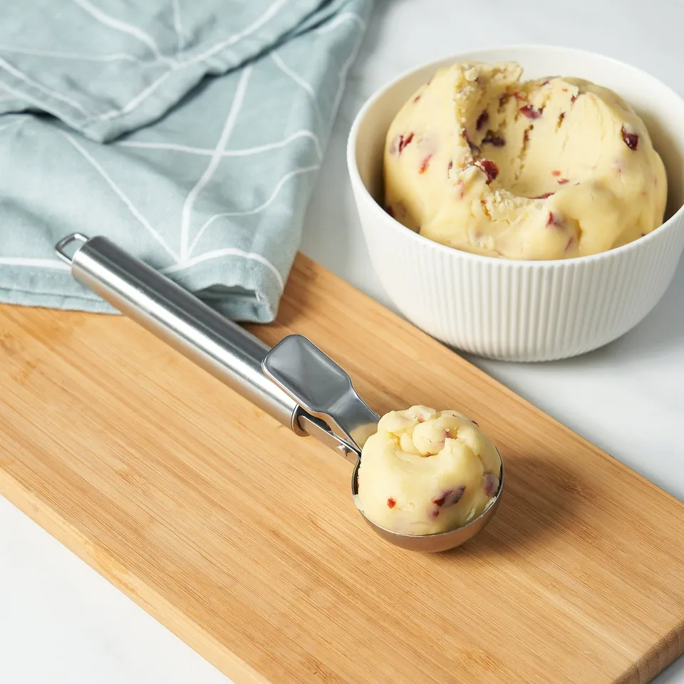 Ice cream scooper in use with bowl on wooden board. Easy-grip handle presses for perfect round scoops.