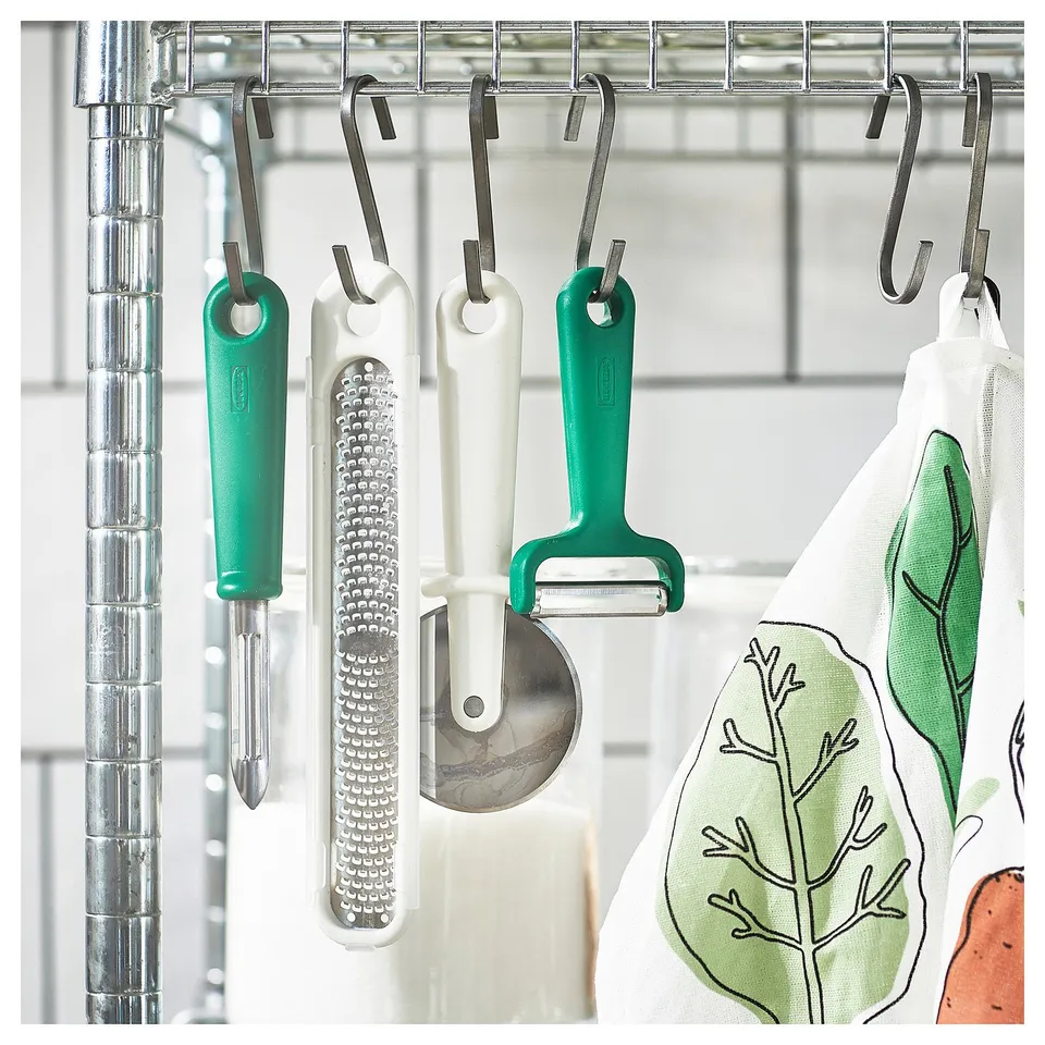 Four kitchen tools hang from a rack: peelers and grater with stainless steel blades and colourful handles.