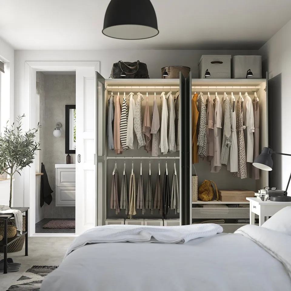Modern bedroom with glass PAX wardrobe, adjustable shelves, mirrored door, bedside lamp, and plant.