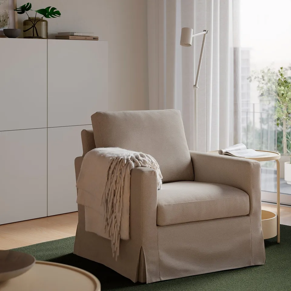 Beige SALTSJÖBADEN armchair with light throw, next to white cabinet and window, creating cosy atmosphere.