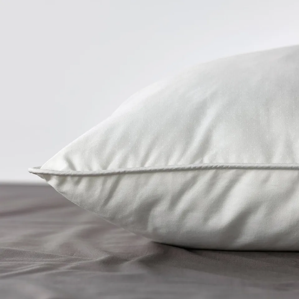 Close-up of a fluffy, white pillow on a bed with soft lighting, highlighting its plush texture and supportive shape.