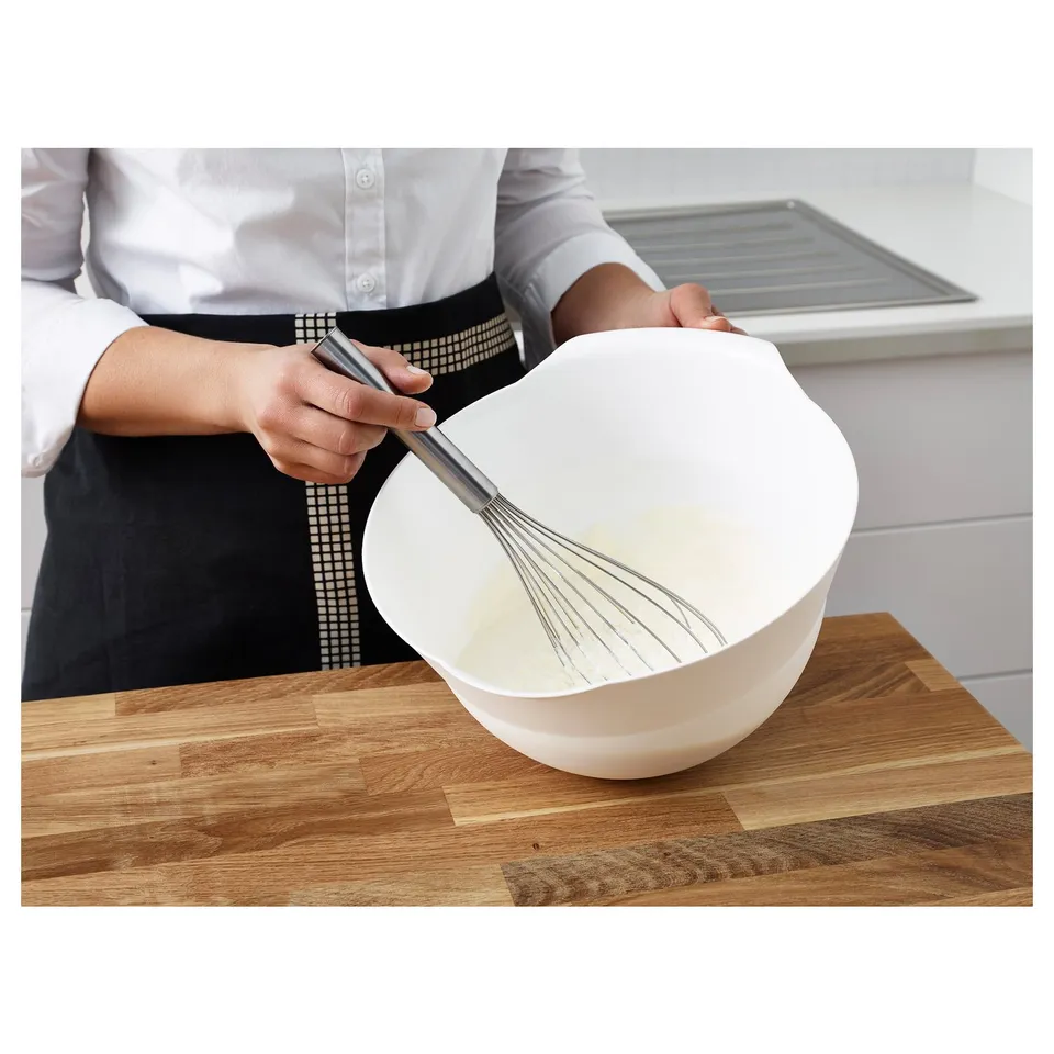 Person whisks ingredients in a white bowl using a metal whisk on a wooden surface.
