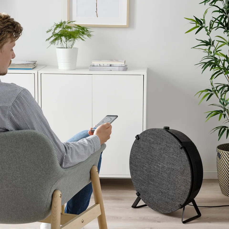 Person sits in grey chair using phone near black air purifier.