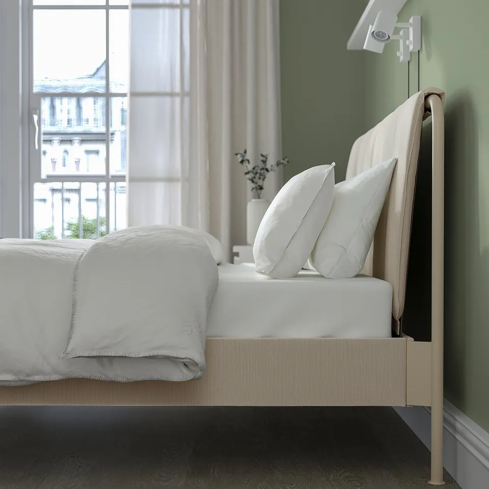 Modern bed with adjustable sides and upholstered headboard, showing white pillows and light beige fabric against a green wall.
