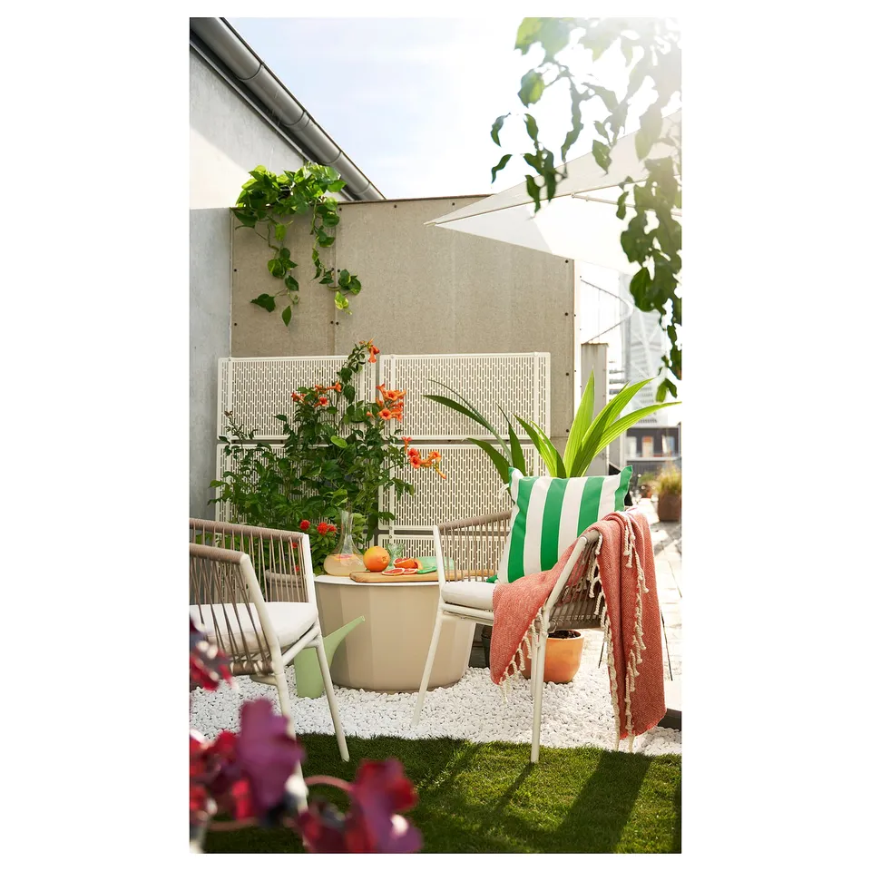 Balcony with green, white, and red decor: wicker chairs, striped cushion, blanket, plants, and pebbles.