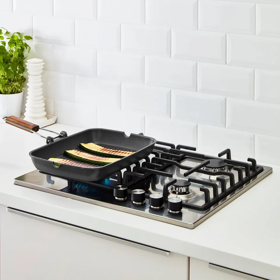 Gas stove with grill pan cooking courgette. Pan has foldable handle and non-stick surface.