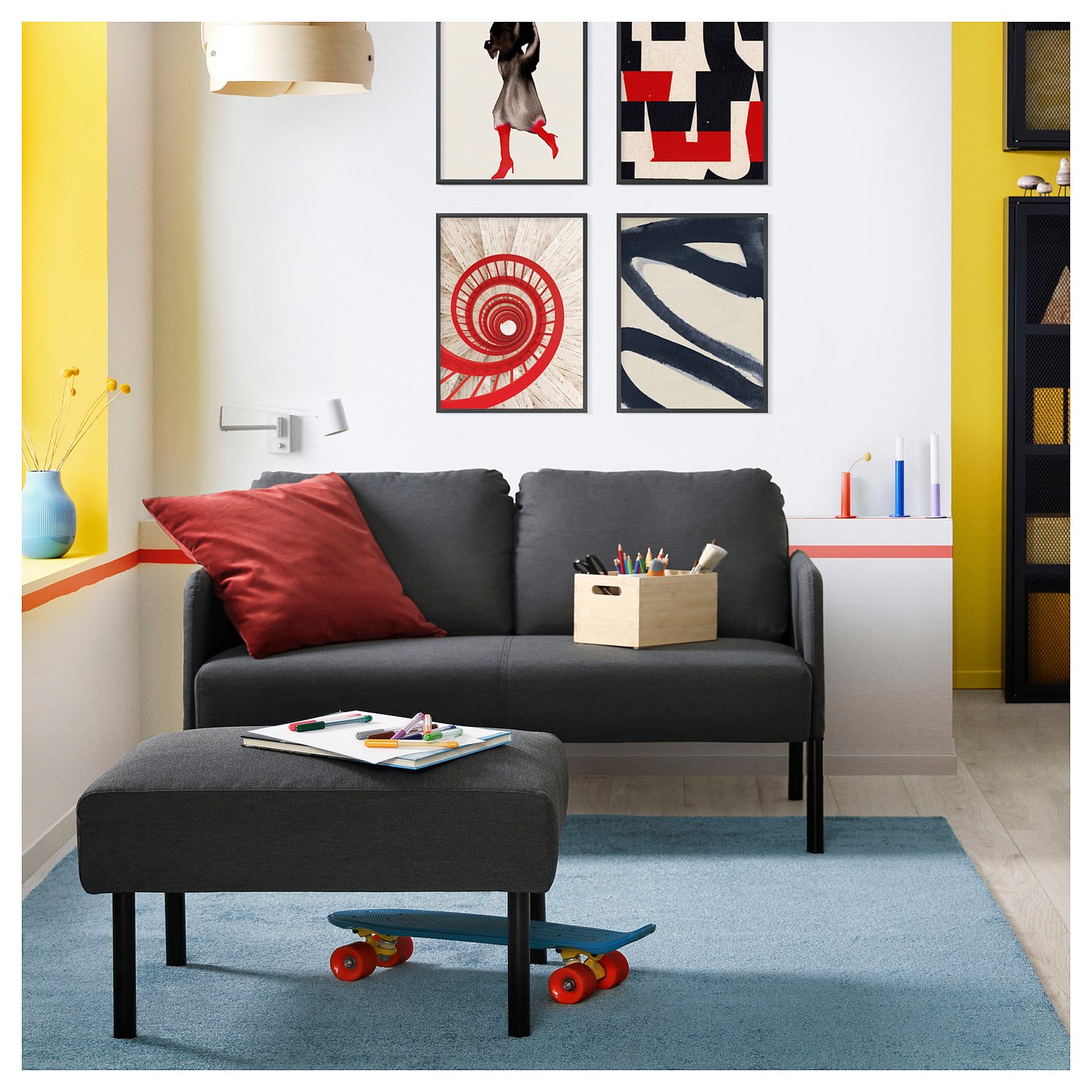 Modern living room with grey GLOSTAD sofa and footstool. Colourful pillows and skateboard coffee table. Wall art, blue rug.