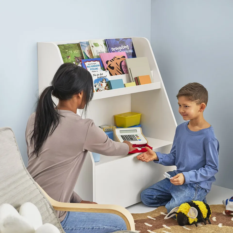 Adult and child use low bookcase with open shelves and drawer, handling books and toys neatly.