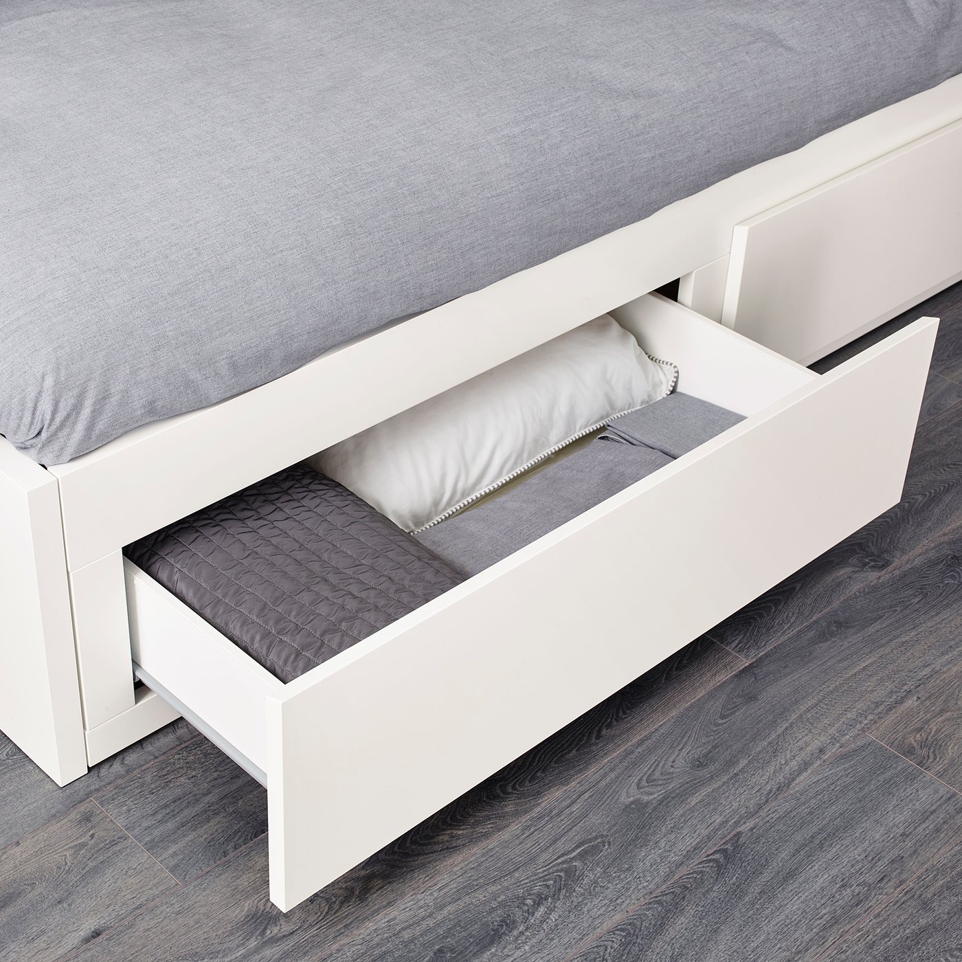 White day-bed with large storage drawers open, revealing mattresses and linens neatly organised.